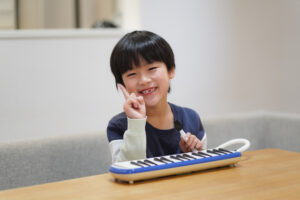 ein kleiner Junge mit dem Melodika-Instrument lächelt verschmitzt in die Kamera.